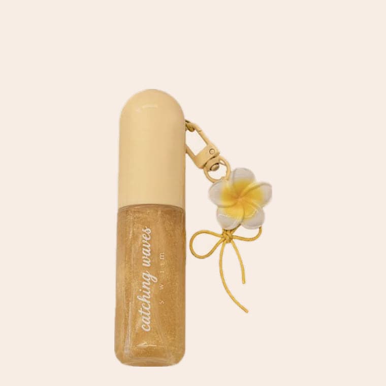 A gold glitter body shimmer on a clip, with a frangipani charm and a ribbon bow